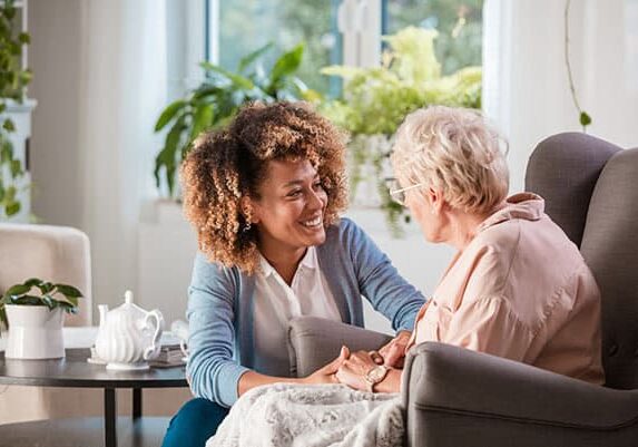 Female home caregiver talking with senior woman, sitting in nursing home and listening to her carefully.