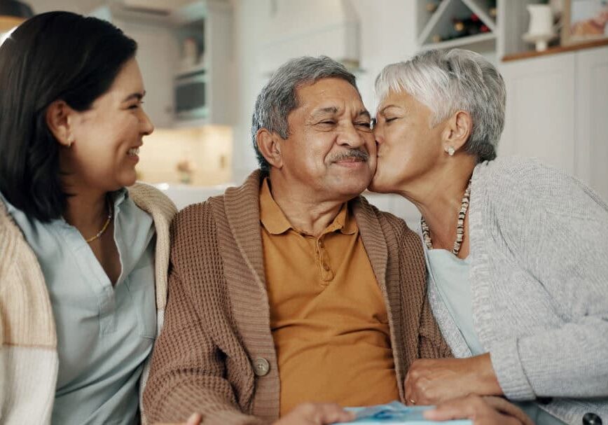 Birthday, gift and senior parents on sofa for celebration, festive event and bonding together at home. Happy family, party and elderly mother and father with daughter for present, surprise and love Avenues Home Care can help alleviate family Caregiver Burnout